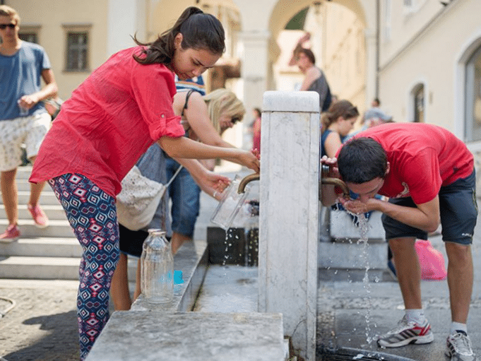 People drinking water from a drinking tap on a square