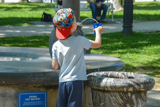 A kid pouring water in a cup in the park